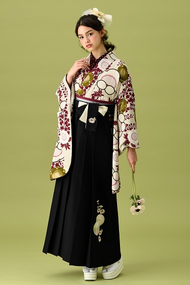 山本寛斎ブランドの、白地にワインレッドの花柄の二尺袖と、黒の袴の女性用卒業式袴を着用した全身写真
