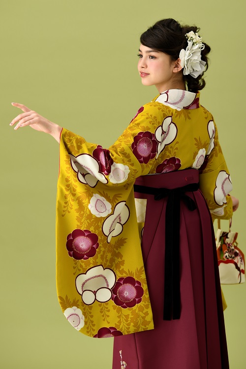 山本寛斎ブランドの、からし地にワインレッドの花柄の二尺袖と、ワインレッドの袴の女性用卒業式袴を着用したアップ写真