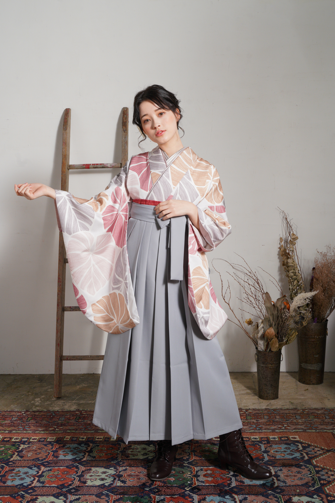 ラフィネモカ（Raffine Mocha）ブランドの、白地にモダンな淡色の花柄の二尺袖と、グレーの袴の女性用卒業式袴を着用した全身写真