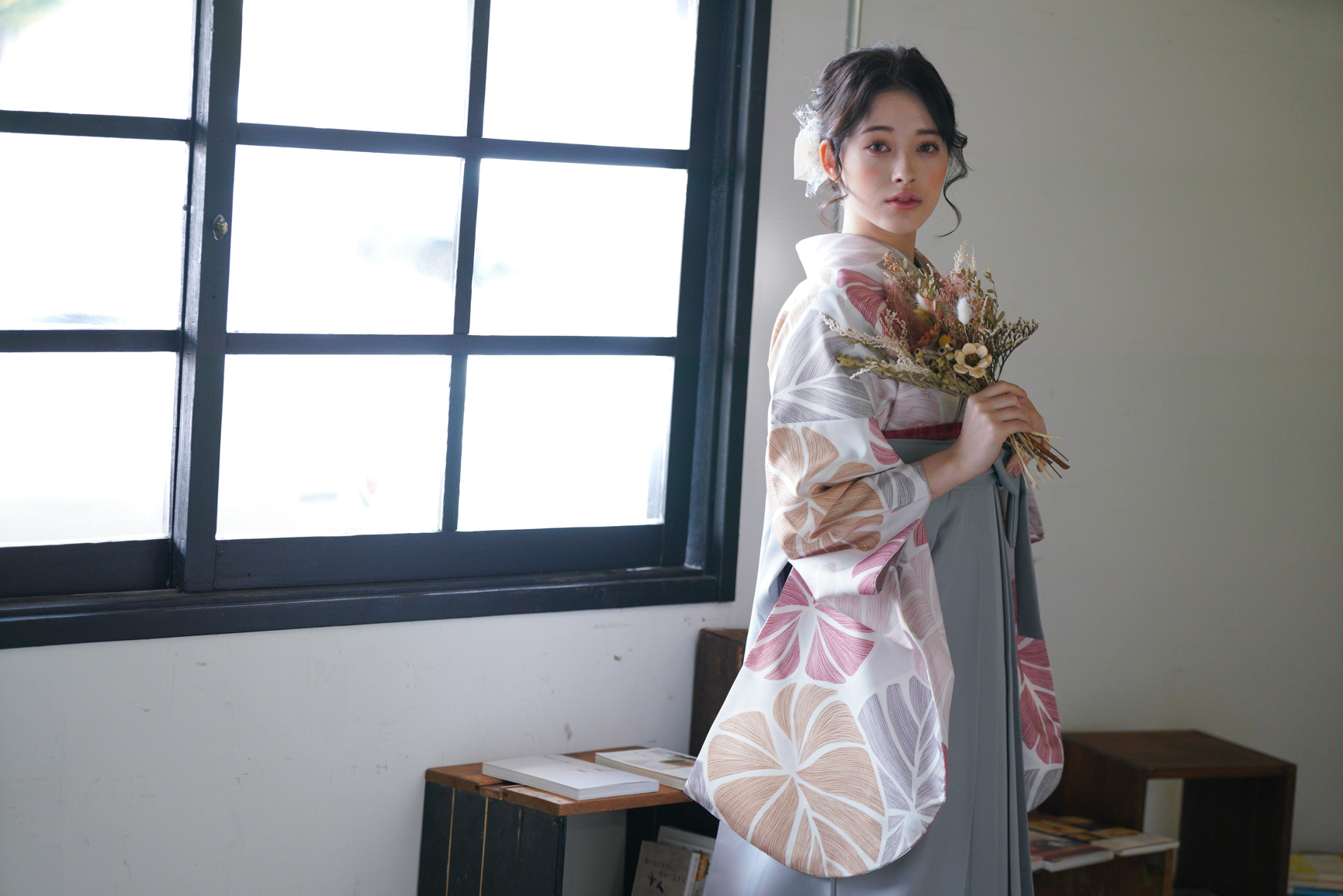 ラフィネモカ（Raffine Mocha）ブランドの、白地にモダンな淡色の花柄の二尺袖と、グレーの袴の女性用卒業式袴を着用した横から見た写真