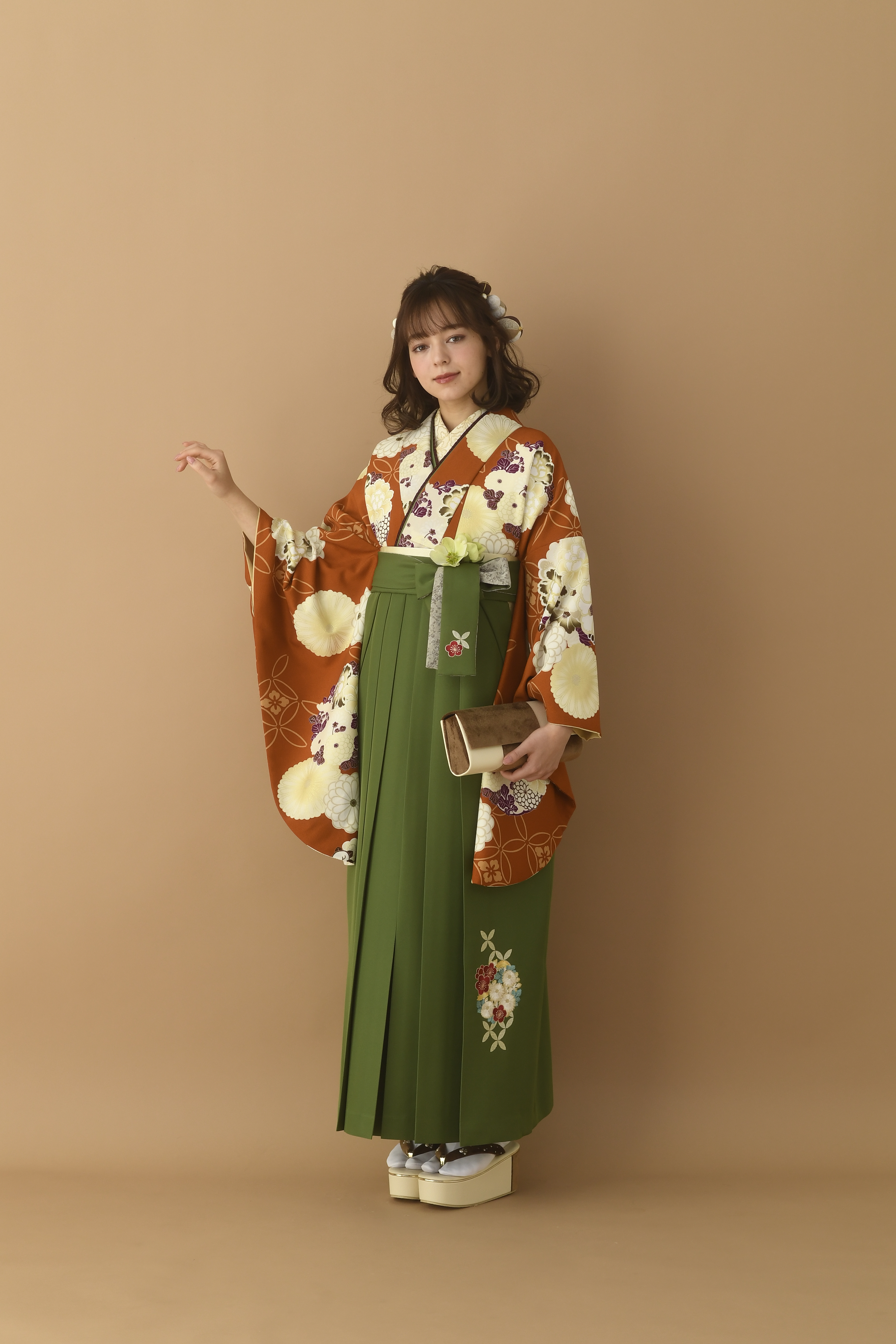 山本寛斎（ヤマモトカンサイ）ブランドの、エンジ地に白の花柄の二尺袖と、緑の袴の女性用卒業式袴を着用した全身写真