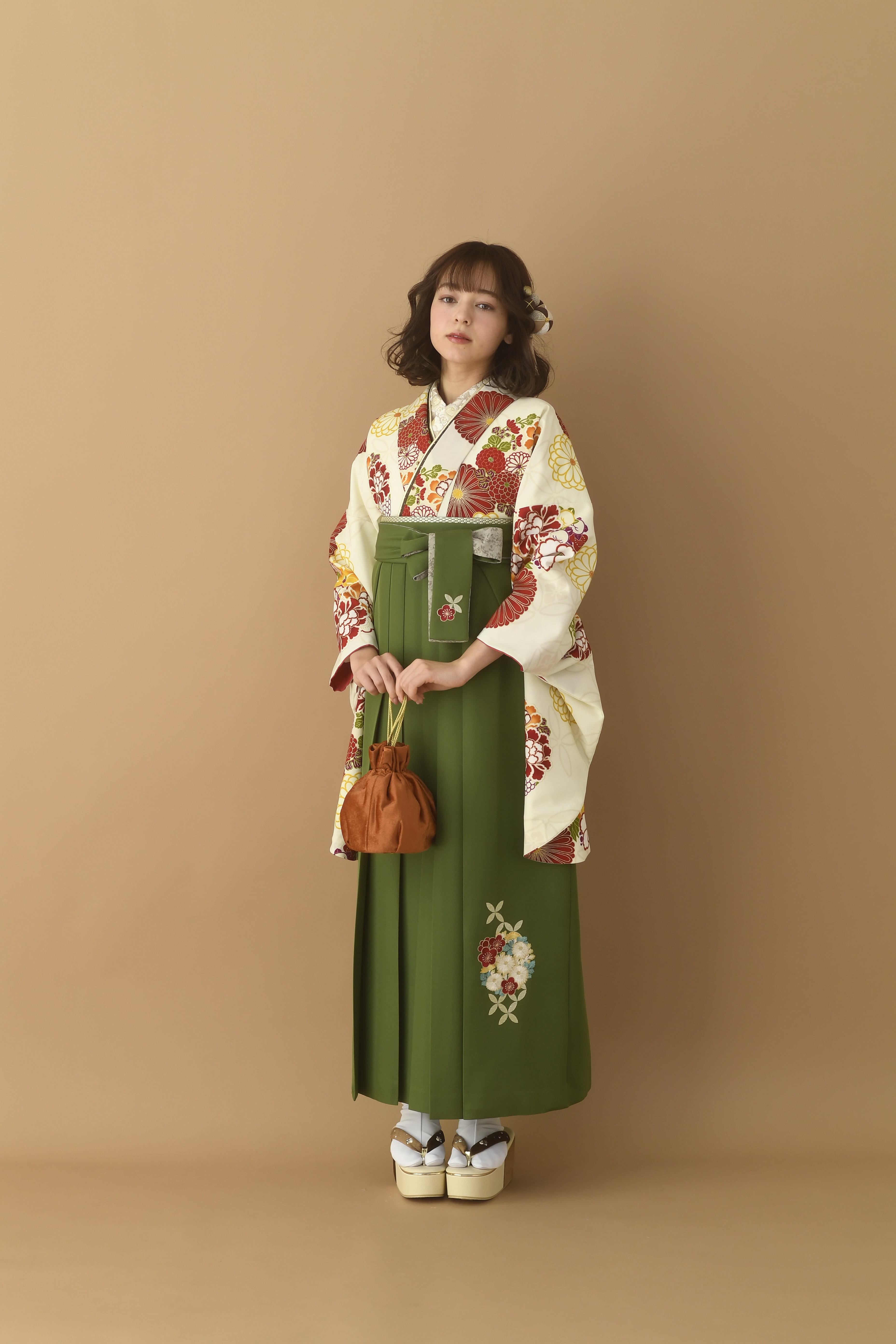 山本寛斎（ヤマモトカンサイ）ブランドの、白地にエンジの花柄の二尺袖と、緑の袴の女性用卒業式袴を着用した全身写真