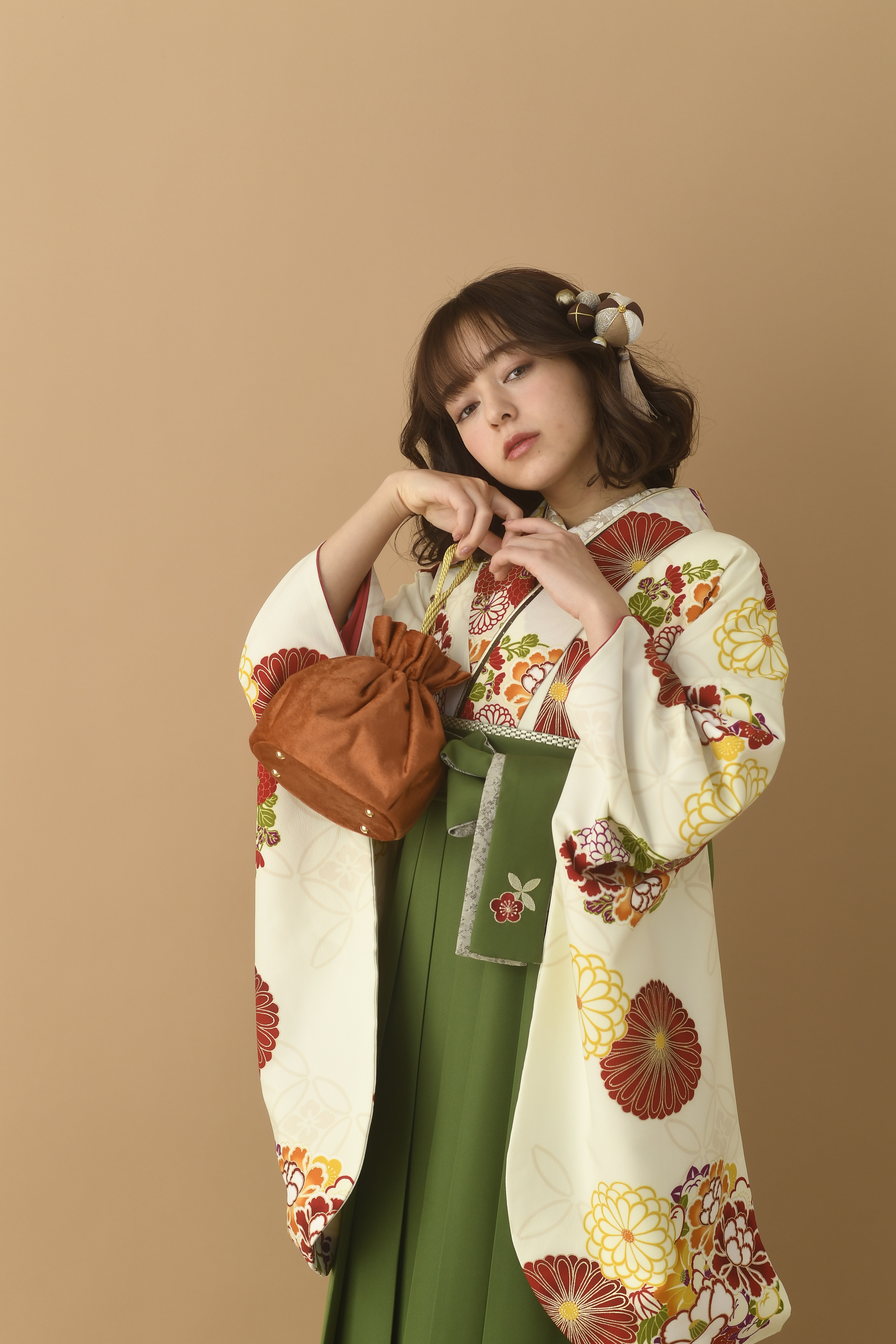 山本寛斎（ヤマモトカンサイ）ブランドの、白地にエンジの花柄の二尺袖と、緑の袴の女性用卒業式袴を着用したアップ写真