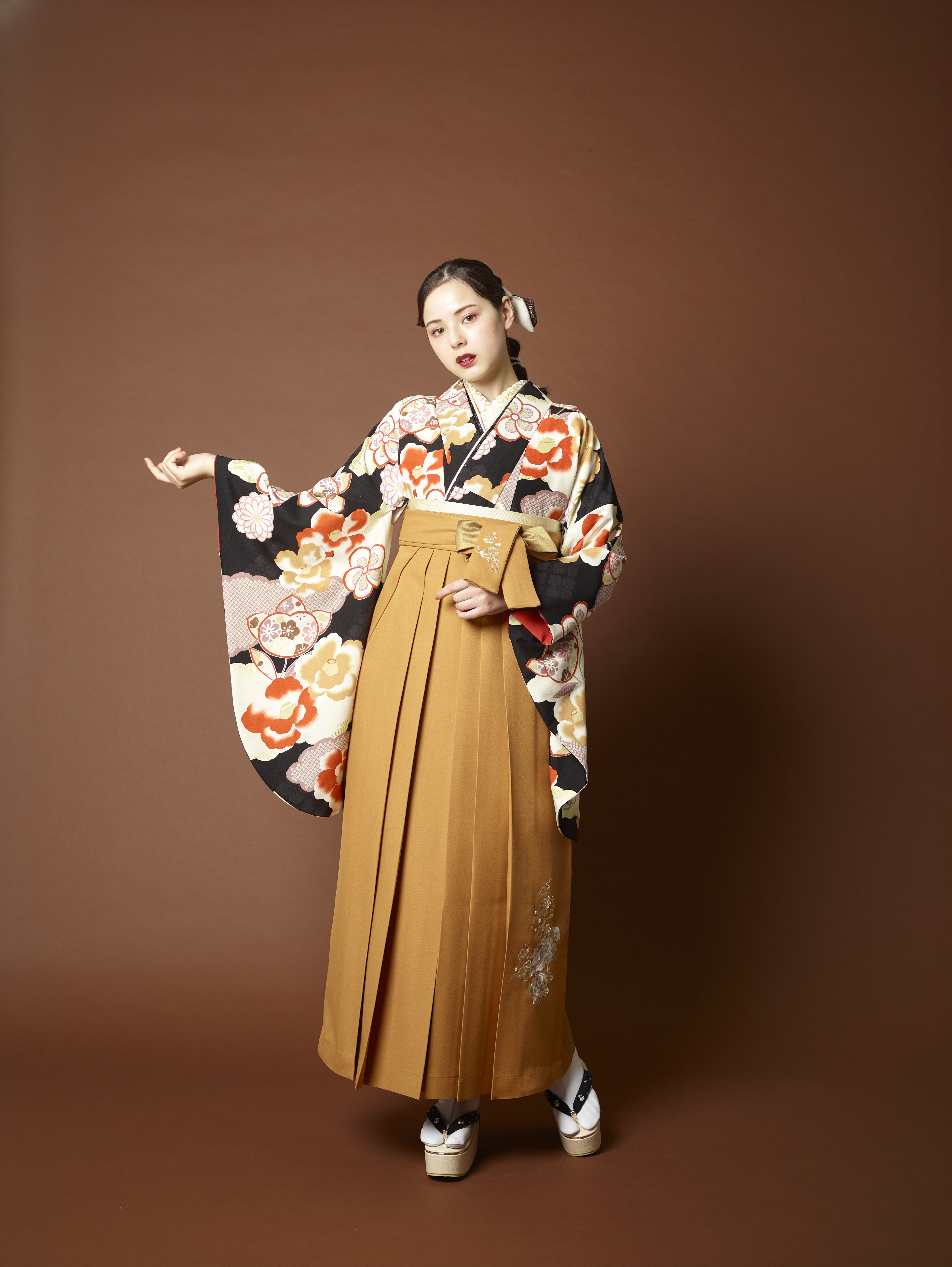 山本寛斎（ヤマモトカンサイ）ブランドの、黒地に白と赤の花柄の二尺袖と、からし色の袴の女性用卒業式袴を着用した全身写真
