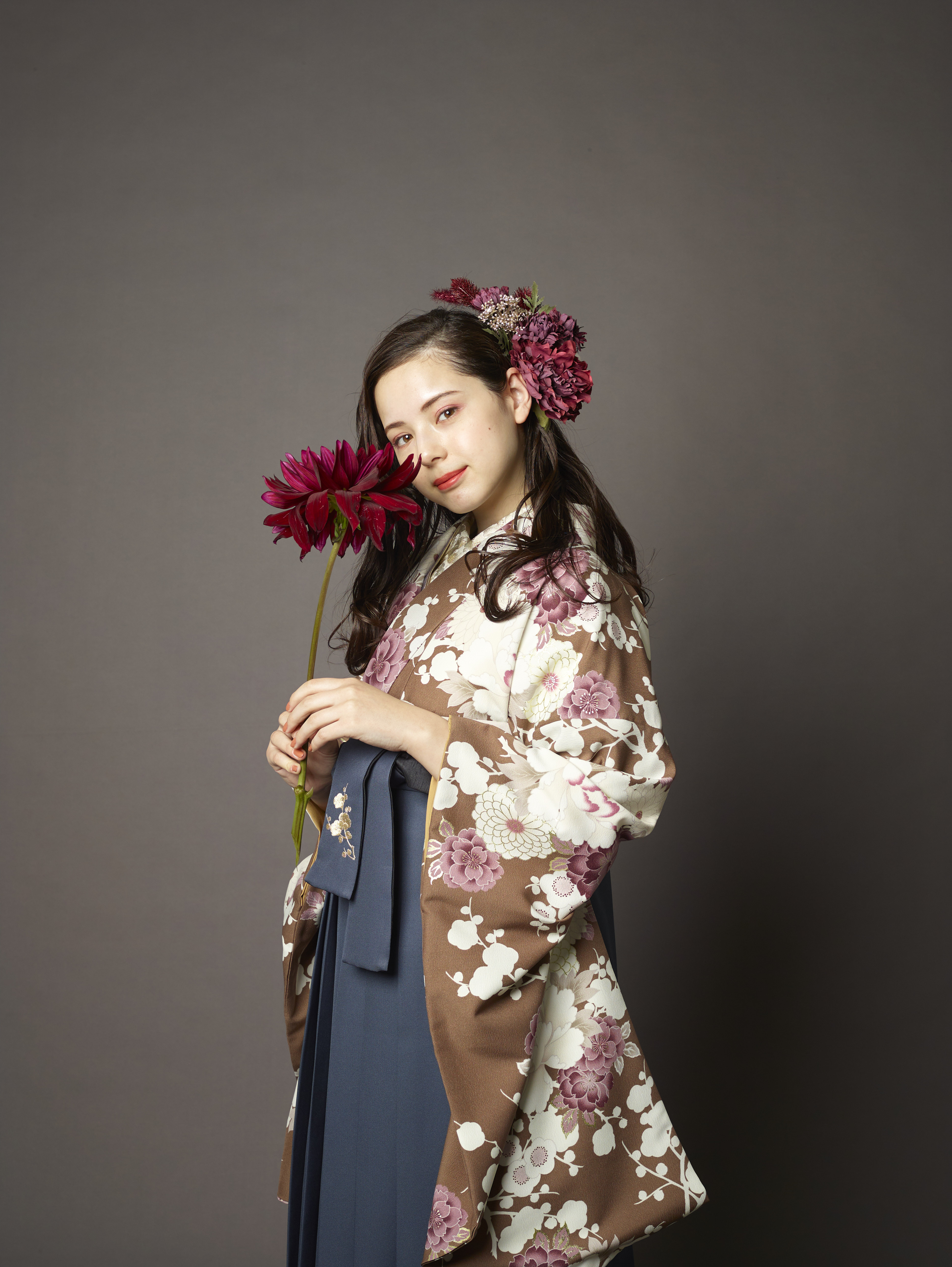 山本寛斎（ヤマモトカンサイ）ブランドの、ブラウン地に白の花柄の二尺袖と、黒の袴の女性用卒業式袴を着用したアップ写真