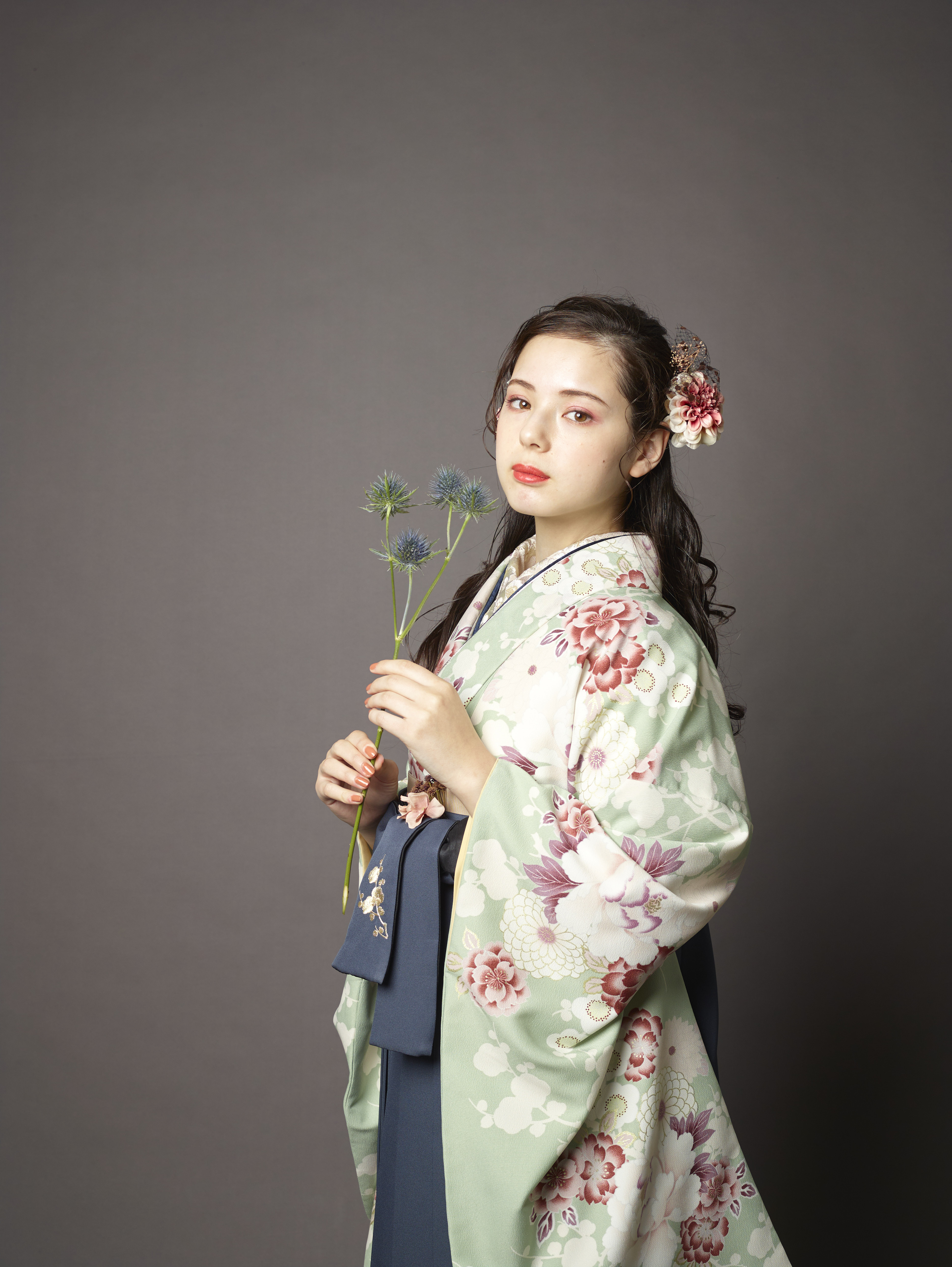 山本寛斎（ヤマモトカンサイ）ブランドの、緑地に白とピンクの花柄の二尺袖と、黒の袴の女性用卒業式袴を着用したアップ写真