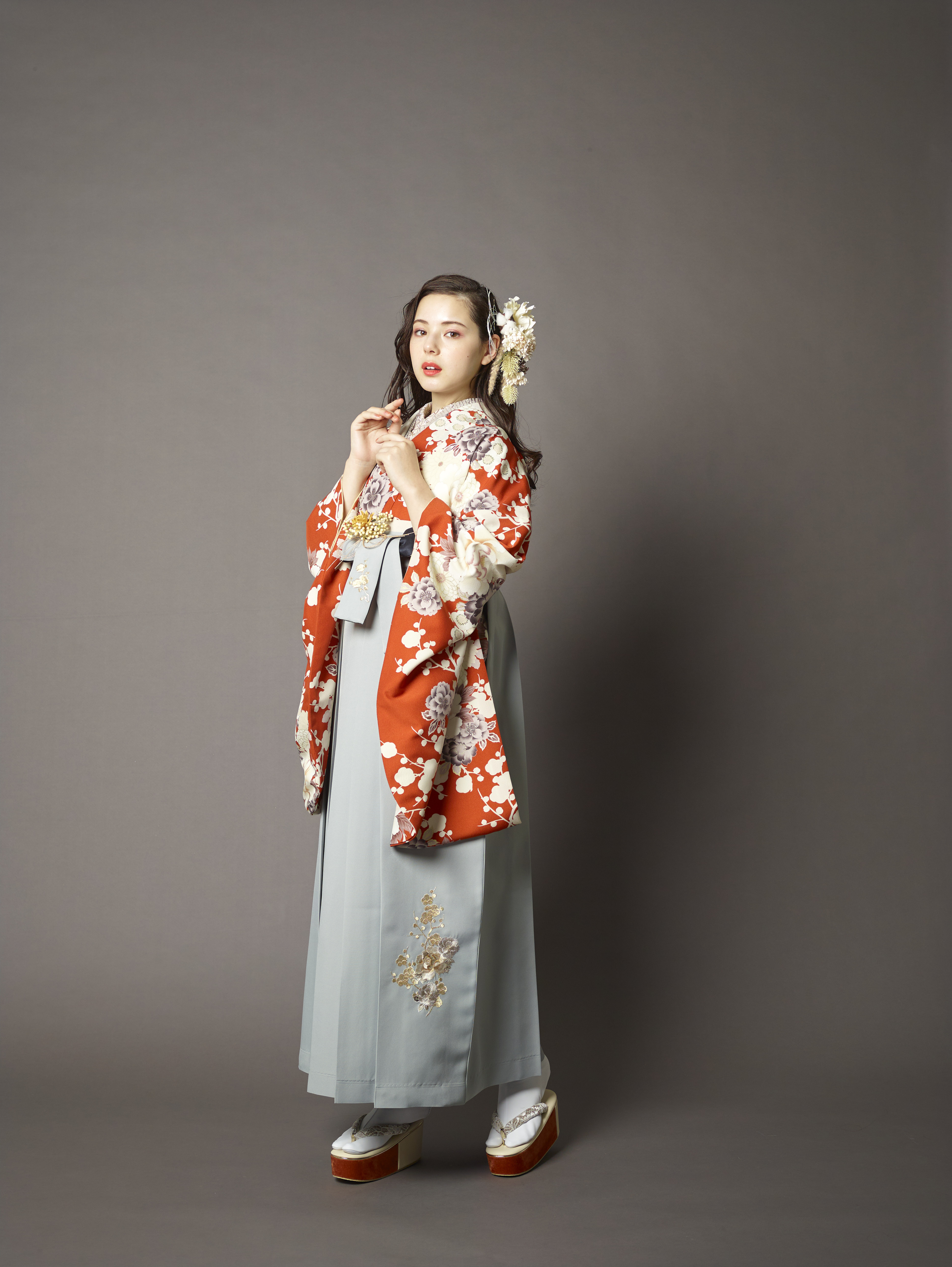 山本寛斎（ヤマモトカンサイ）ブランドの、テラコッタ地に白の花柄の二尺袖と、グレーの袴の女性用卒業式袴を着用した全身写真