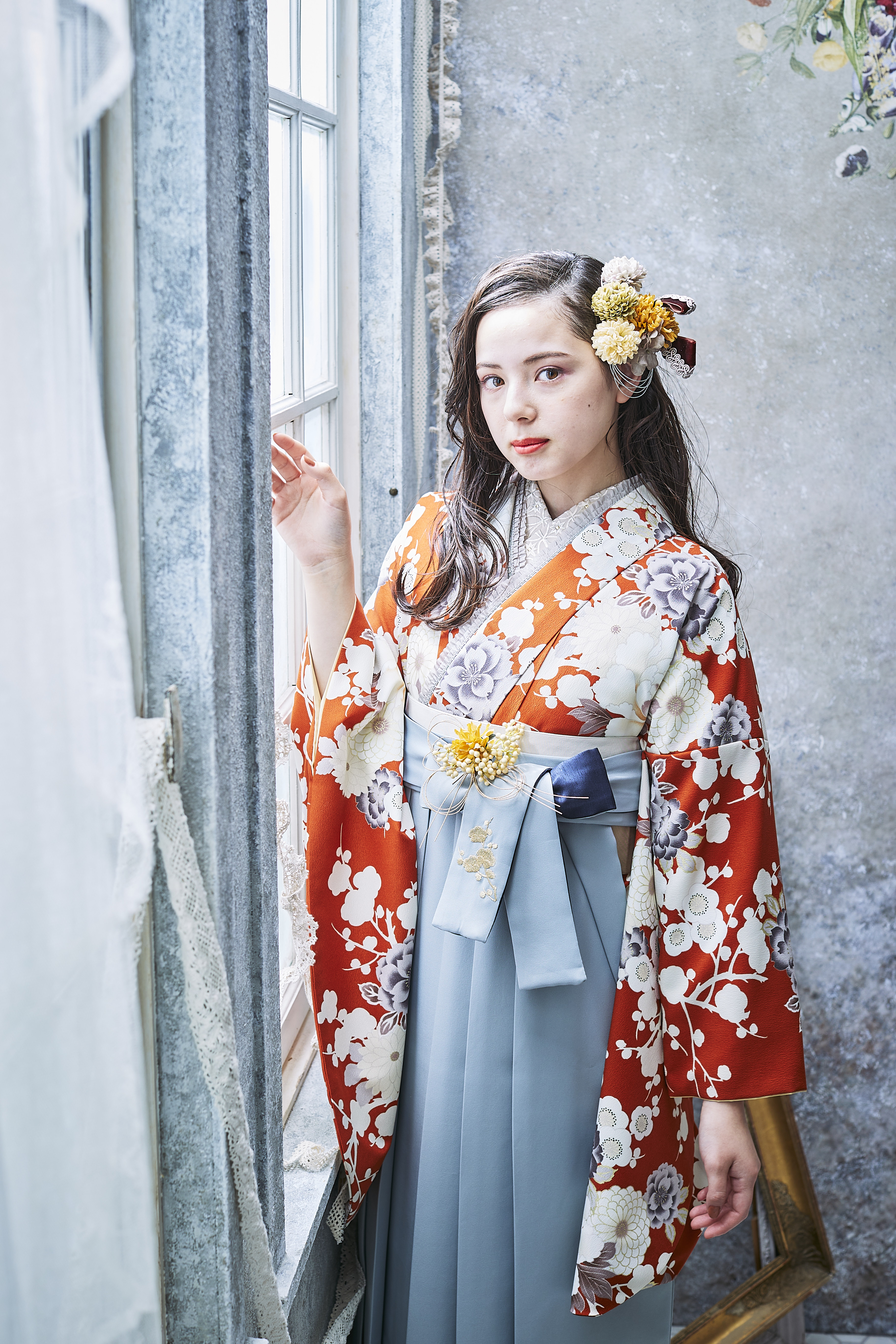 山本寛斎（ヤマモトカンサイ）ブランドの、テラコッタ地に白の花柄の二尺袖と、グレーの袴の女性用卒業式袴を着用したアップ写真