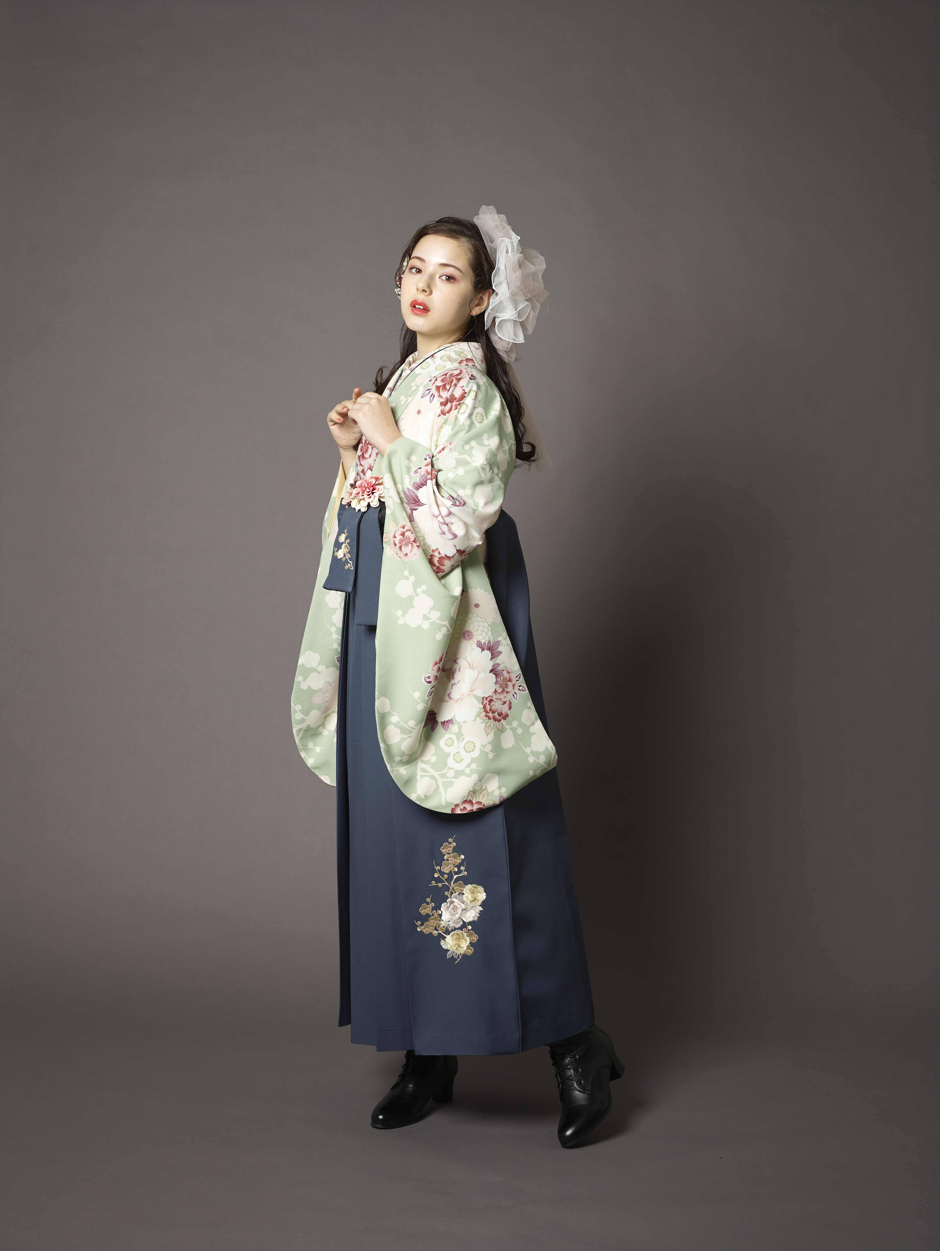 山本寛斎ブランドの、ミントグリーン地に白とピンクの花柄の二尺袖と、黒の袴の女性用卒業式袴を着用した全身写真