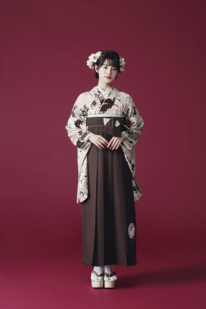 NATURAL BEAUTYブランドの、ブラウン地に花柄の二尺袖と、ブラウンの袴の女性用卒業式袴を着用した全身写真