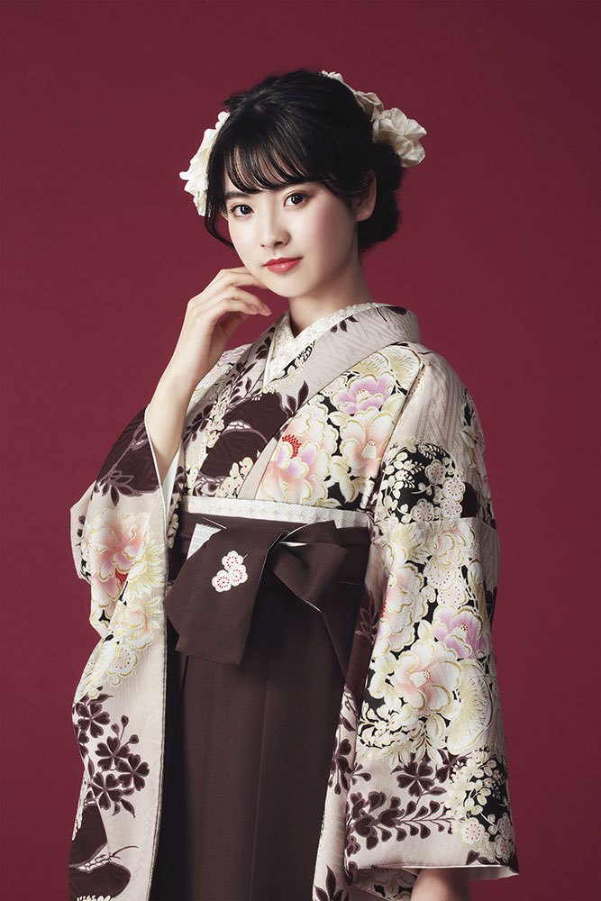 NATURAL BEAUTYブランドの、ブラウン地に花柄の二尺袖と、ブラウンの袴の女性用卒業式袴を着用したポートレート