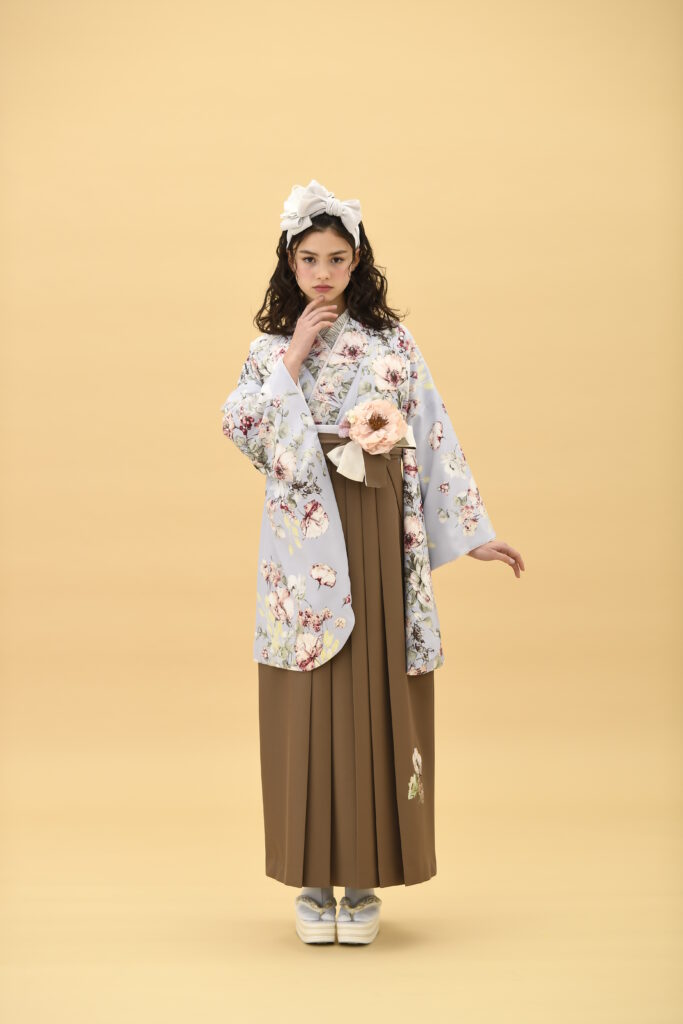 SUGAR KEIブランドの、すみれ色地に花柄の二尺袖と、ブラウンの袴の女性用卒業式袴を着用した全身写真